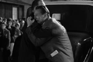 Why Victory Sometimes Feels Sad in Cinema 2 A powerful black-and-white cinematic shot from Schindler's List showing Liam Neeson as Oskar Schindler weeping and deeply embracing another man next to a car. Surrounded by onlookers, his breakdown highlights a heartbreaking sense of regret and the profound sorrow that can accompany a humanitarian victory.